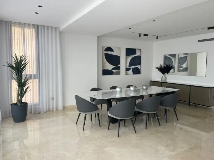 Modern dining room with marble-top table, gray chairs, abstract navy wall art, and large mirror in a minimalist interior